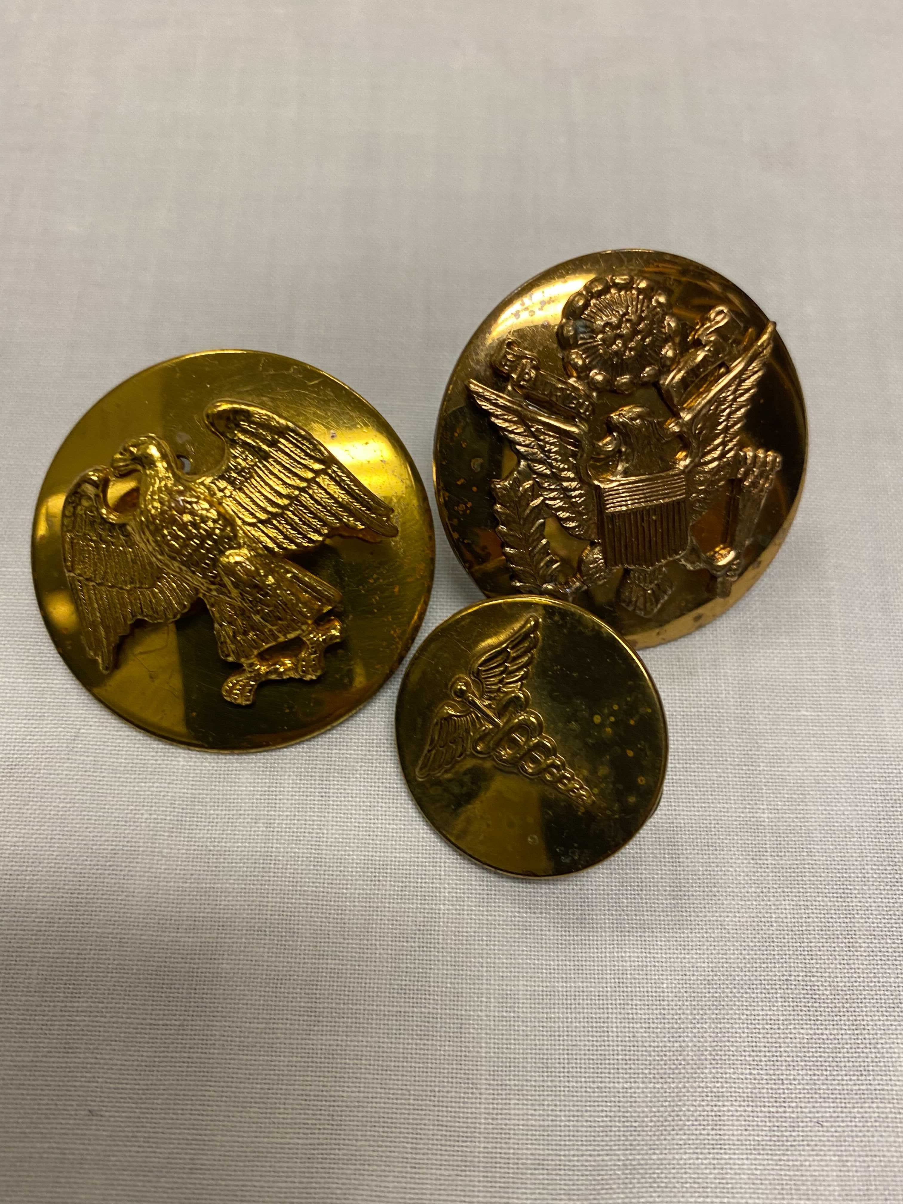 Three brass pills and badges, one with an eagle, another with an eagle and crest, and finally a smaller pin of the medical symbol, Caduceus.